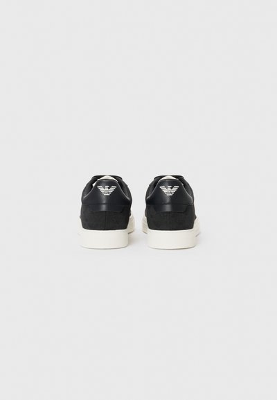 Baskets noires avec un panneau arrière texturé, semelle blanche et détail de marque au niveau du talon. Conception à lacets avec finition lisse.