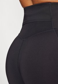 Magas derekú fekete leggings rugalmas anyagból, látható varrásokkal és sima textúrával, testhez simuló kialakítással.