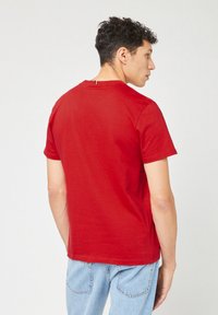 Rode katoenen T-shirt met een ronde hals, korte mouwen en een recht model. Heeft een klein luslabel aan de achterkant van de hals.