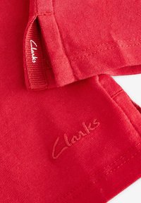 Rode stof met een gladde textuur, voorzien van een gestikt "Clarks" logo in bijpassend draad. Schone randen en minimalistischer ontwerp.