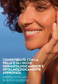 Primo piano di un volto sorridente con capelli ricci su uno sfondo blu, che mette in risalto una pelle chiara e una mano che tocca delicatamente la guancia.