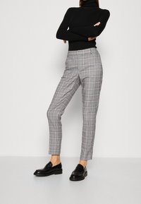 Šedé kostkované kalhoty s úpravou na míru, s jemným vzorem a hladkou texturou. Kombinovány s černými mokasínami a černým rolákem.