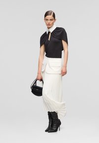 Black short-sleeve top with a white collar, pleated white skirt, black heeled boots, and a small black handbag.