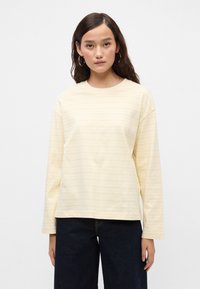 Κίτρινη ριγέ μπλούζα με μακριά μανίκια από μαλακό ύφασμα, με στρογγυλή λαιμόκοψη και άνετη εφαρμογή. Φοριέται με σκούρα τζιν παντελόνια.