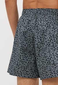 Boxers à motif en tissu bleu-gris avec un imprimé floral en marine foncé. Taille élastique avec une coupe décontractée, texture douce.