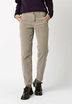 Person wearing beige corduroy pants with hands in pockets, dark purple sweater, brown socks, and black lace-up shoes.