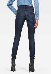 Jeans ajustados de denim azul oscuro, con un diseño ceñido, bolsillos traseros y ligeros desgastes. Combinados con botas de tacón alto negras.