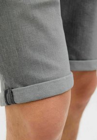 Grijze denim shorts met opgerolde cuffs, met een soepele textuur en klassieke snit. Close-up weergave die de stofstructuur en stiksels benadrukt.