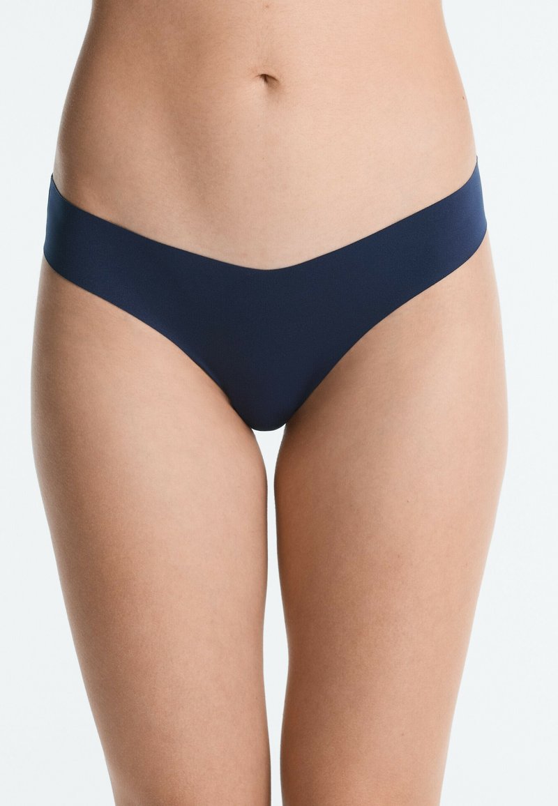 Femme portant un sous-vêtement bikini bleu marine sans couture taille basse, visible de la taille jusqu’au milieu de la cuisse sur fond clair.
