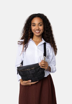 Borsa in pelle nera con texture intrecciata, chiusura con zip e tracolla regolabile, tenuta da una persona che indossa una camicia bianca e una gonna marrone.