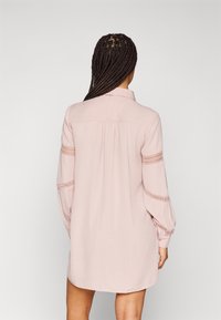 Hellrosa Hemdblusenkleid mit Kragen, langen Ärmeln und Häkelakzenten an den Ärmeln, bietet eine lockere Passform und eine Rückenfalte.