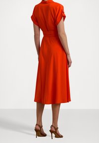 Orange klänning med korta uppvikta ärmar, åtsittande midja, flödande kjol och slät textur, i kombination med bruna klacksandaler.