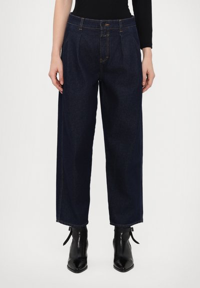 Jean large bleu marine avec plis sur le devant, en denim. Équipé d'une fermeture à bouton et zip, et de surpiqûres dorées contrastées.