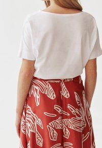 T-shirt bianco a maniche corte abbinato a una gonna rossa con motivi astratti bianchi. La t-shirt ha una vestibilità comoda e un collo rotondo.