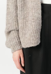 Světlé šedé pletené cardigan s texturou a žebrovaným designem, s oversized rukávy, v kombinaci s černými hladkými kalhotami.