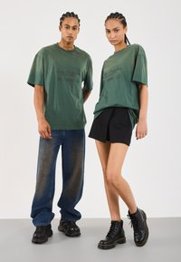 To modeller med fletninger iført matchende grønne "Los Angeles" t-shirts; den ene i blå jeans og sneakers, den anden i et sort nederdel og støvler.