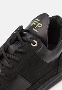 Svarta sneakers med en kombination av slät läder och texturerad mocka. Funktioner inkluderar svarta snörningar, metallöglor och en grön logotyp på tungan.