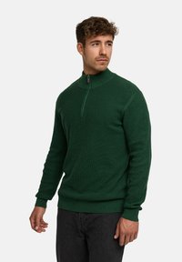 Grøn strikket sweater med høj krave og kvart-zip lukning. Har ribbede manchetter og kant, struktureret stof og tætsiddende design.