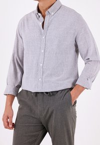 Ljust grå skjorta med en subtil struktur, långa ärmar uppvikta vid ärmsluten och en strukturerad krage. Matchad med grå byxor.