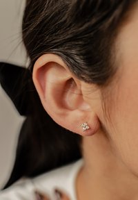 Pendientes de plata con un diseño floral, que presentan cuatro pequeños acentos similares a diamantes, con un primer plano de la oreja de una mujer.