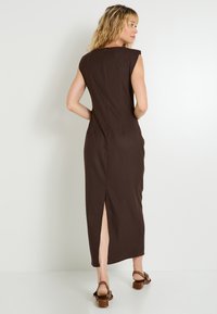 Vestido maxi sin mangas de color marrón con una silueta ajustada, que presenta una abertura en la parte posterior y un cierre de cremallera invisible. Textura de tela suave.