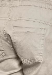 Beige bomullsshorts med en platt bakficka, synliga sömmar och en avslappnad midja. Tyget har en lätt struktur.