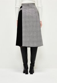 Woman wearing a knee-length skirt with gray plaid and black pleated panels, paired with black knee-high boots and a white sweater.