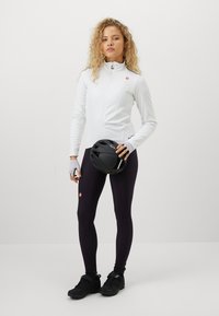 Veste zippée blanche, casque de vélo noir, chaussures de sport noires et leggings violet foncé. Tissu lisse avec une coupe ajustée. Détail du logo rouge.