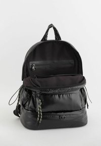 Czarna plecak z błyszczącym wykończeniem, o przestronnym wnętrzu, z wieloma zapinanymi na zamek kieszeniami i kolorowymi sznurkami do ściągania.