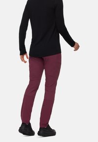 Bordeauxkleurige outdoor broek met een taps toelopende pasvorm, verstevigde knieën en zijzakken, gecombineerd met een zwart langmouwtop en zwarte wandelschoenen.