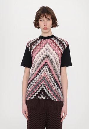 Graphic t-shirt featuring a chevron pattern in pink, black, and cream, with short black sleeves and a crew neckline.