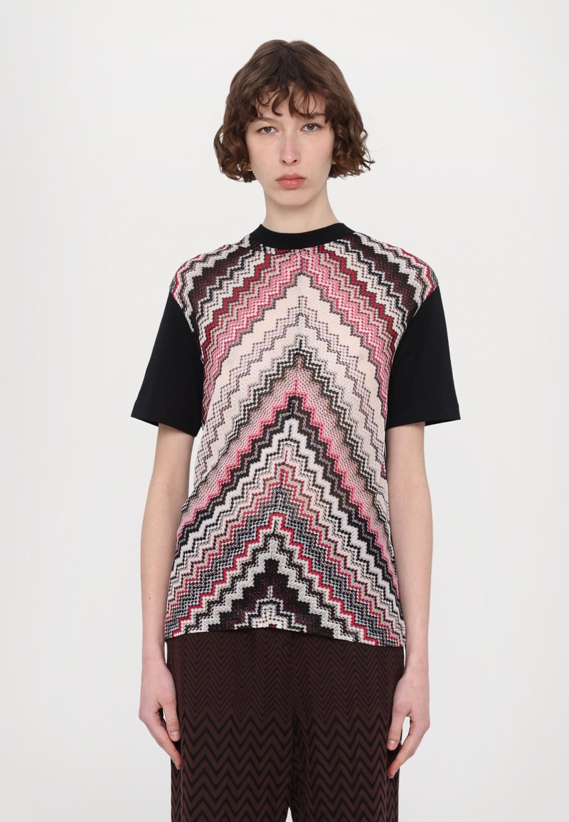 Camiseta gráfica con un patrón de Chevron en rosa, negro y crema, con mangas cortas negras y cuello redondo.