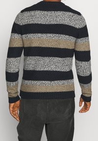 Pletený svetr s proužky v námořnické modři, šedé a béžové barvě, s texturovanou látkou, kulatým výstřihem a žebrovanými manžetami a lemem. Viditelné švy a tkané detaily.