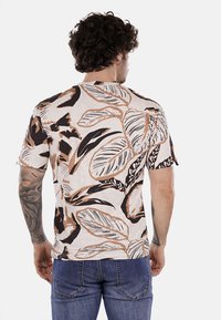 Camisa de manga corta hecha de tela ligera, con una base crema y grandes estampados de hojas tropicales en marrón y negro. HEM recto y corte relajado.