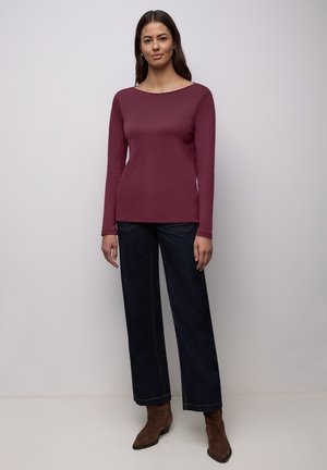 Burgundy long-sleeve shirt in a soft fabric, round neckline, paired with dark wide-leg denim and brown ankle boots.