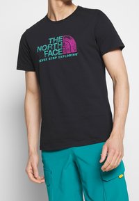 Svart bomullströja med en färgglad grafisk tryck av "The North Face"-logotypen och text, rund hals och korta ärmar.