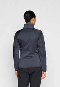 Veste à manches longues, de couleur bleu marine foncé, avec un col haut, une texture lisse et une coupe ajustée, agrémentée de panneaux contrastants aux épaules.