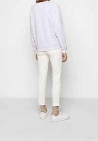 Sweat-shirt lavande clair avec poignets côtelés, associé à un pantalon blanc ajusté et des baskets blanches, vu de dos sur un fond uni.