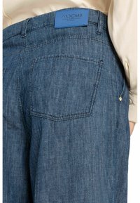 Donkerblauwe denim jeans met een gemêleerd oppervlak, voorzien van een achterzak en een blauwe merklabel bij de taille. Eenvoudige stiksels accentueren het ontwerp.