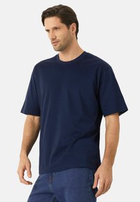 Námořnická modrá tričko s krátkým rukávem v uvolněném střihu, vyrobené z měkké tkaniny s kulatým výstřihem a hladkou texturou. Akcentuje minimalistický design.
