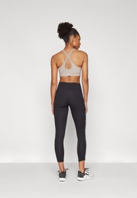 Sports-bh i lys brun med en design med stropper på ryggen; kombinert med svarte leggings som har en hvit sidestripe; glatt, elastisk stoff.