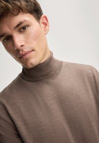 Brauner, gerippter Rollkragenpullover mit weichem Material und figurbetontem Design, hohem Kragen und minimalistischem Stil.