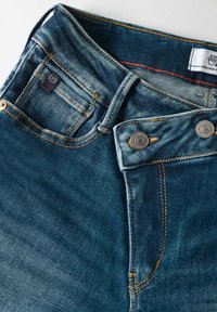 Jeans en denim bleu foncé, avec une taille haute, des boutons en métal argenté, des coutures contrastées et un design classique à cinq poches.
