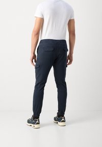Marinblå joggerbyxor med elastiskt midjeband, sidofickor och cargofickor på låren, i kombination med blå och vita sneakers.