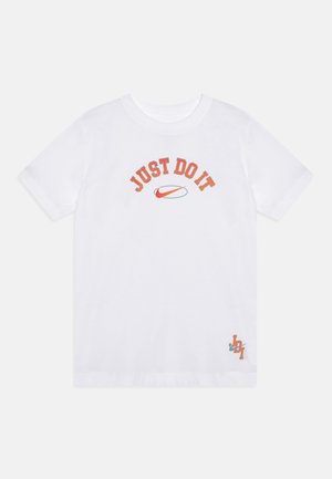 Biała koszulka z krótkim rękawem z pomarańczowym napisem "JUST DO IT" i czerwonym logo Nike swoosh na środku oraz małym logo "JD1" w prawym dolnym rogu.