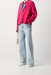 Różowy sweter z prążkowanej dzianiny, jasnoniebieskie spodnie typu wide-leg, białe buty z szpiczastym noskiem oraz biała torba na rami�ę z uchwytem w stylu paska.