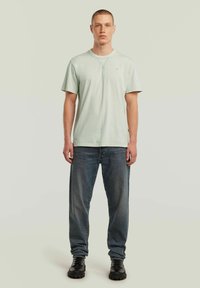 T-shirt in cotone verde chiaro con colletto rotondo, maniche corte e logo sottile. Abbinato a jeans in denim blu e scarpe chunky nere.