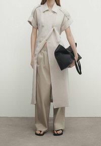 Jasnobeżowy płaszcz lniany z krótkimi rękawami i podwójnymi guzikami, zestawiony z beżowymi spodniami w szerokiej nogawce i czarną miękką torbą na ramię.