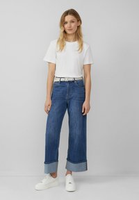 Witte katoenen t-shirt, blauwe wijde jeans met opgerolde zoom en witte sneakers. Eenvoudig ontwerp met een gladde textuur en geen zichtbare patronen.