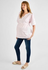 Šviesiai rožinė nėštumo palaidinė su V formos iškirpte, susirinkusia liemeniu ir pūstu rankovėmis, derinama su tamsiai mėlynomis siaurėjančiomis džinsomis ir kreminėmis plokščiosiomis sandalais.